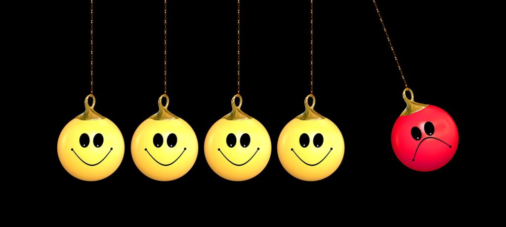 5 Newton pendulum balls, 4 with yellow smiley faces but the last one on the right is red and sad